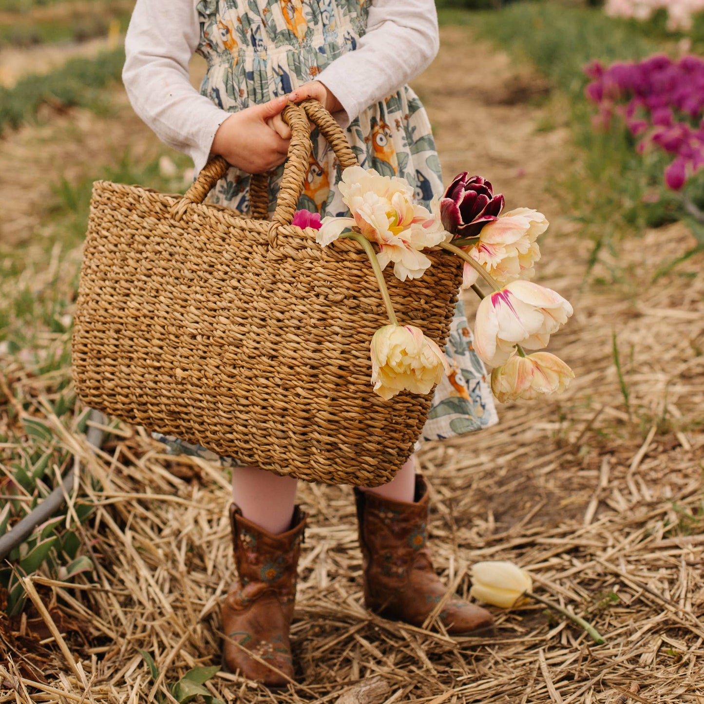 Person holding a woven basket with flowers in a field