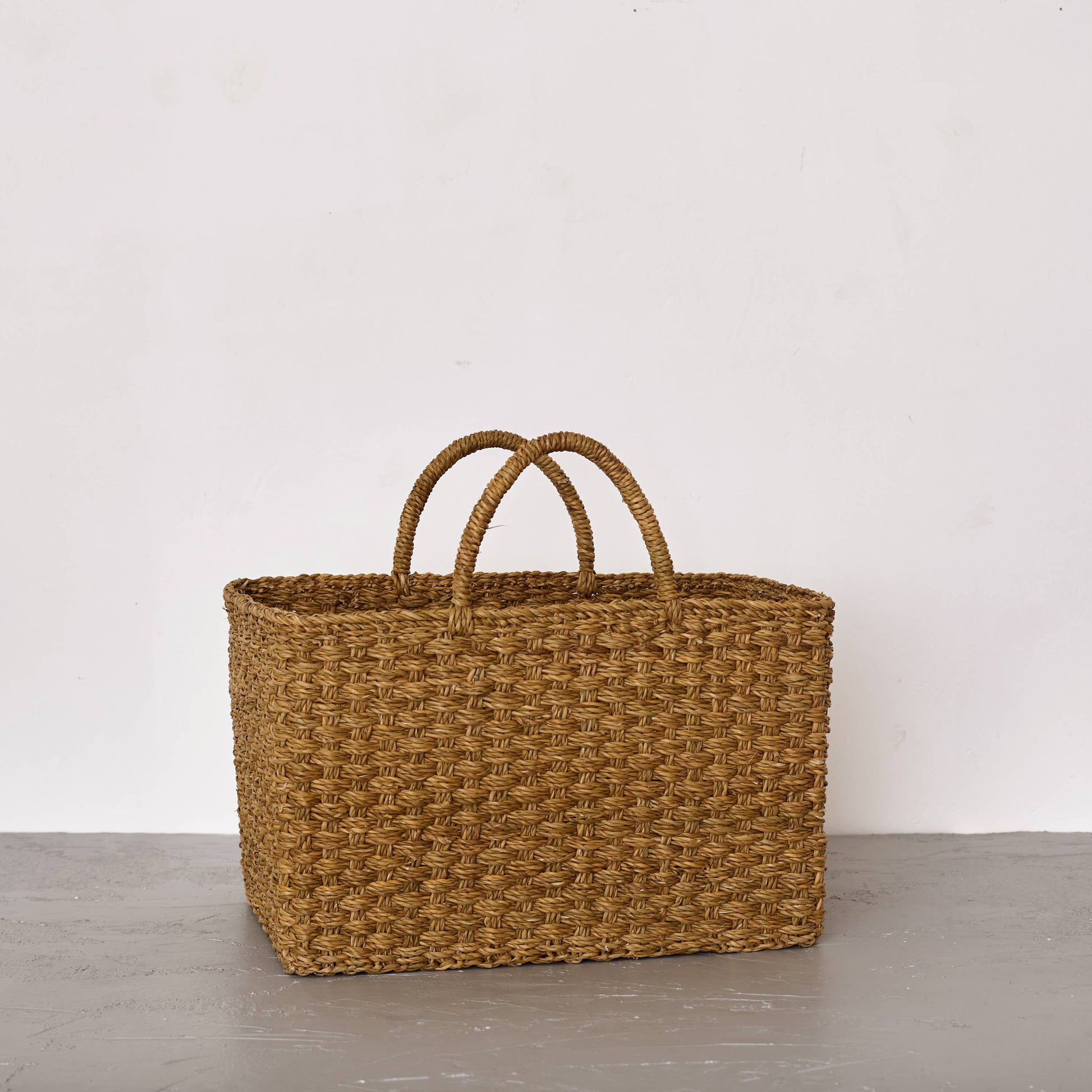 Woven basket with handles on a gray surface and white background