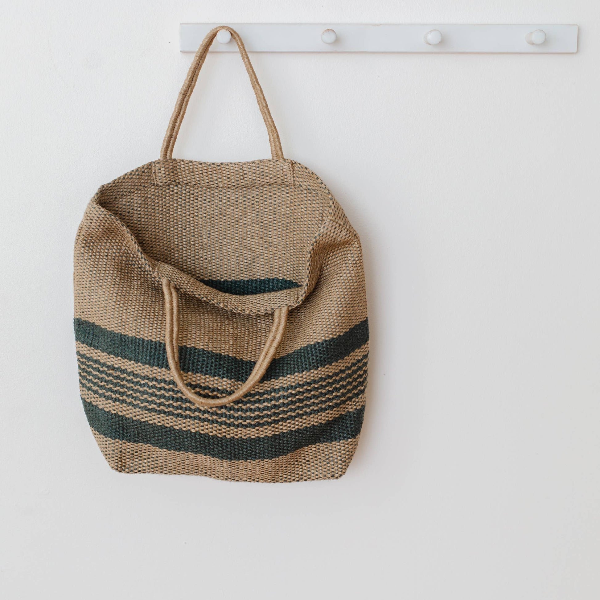 Woven bag with striped pattern hanging on a white wall.