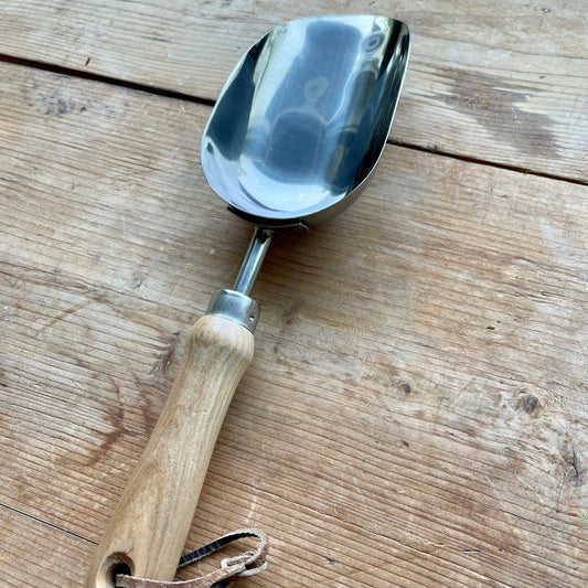 Metal scoop with wooden handle on a wooden surface