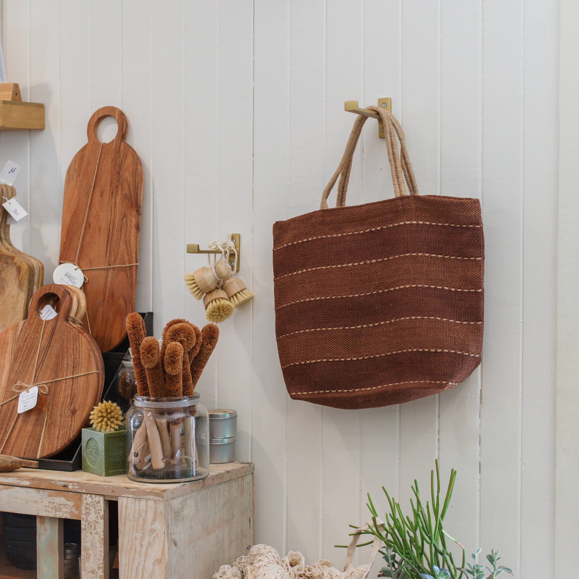 Decorative items including a woven basket, cutting boards, and plants on a wooden shelf against a white wall.
