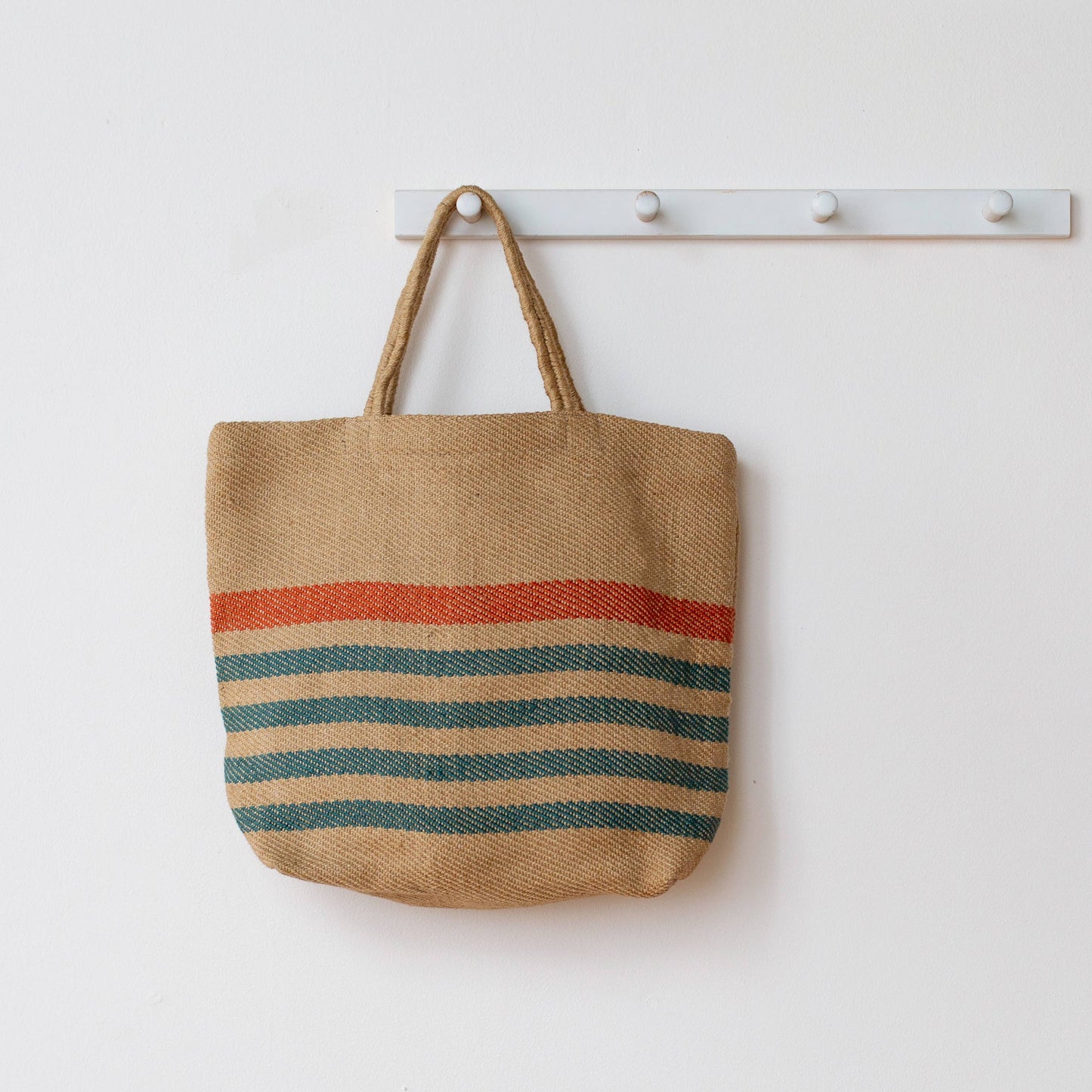 Jute bag with colorful stripes hanging on a white wall.