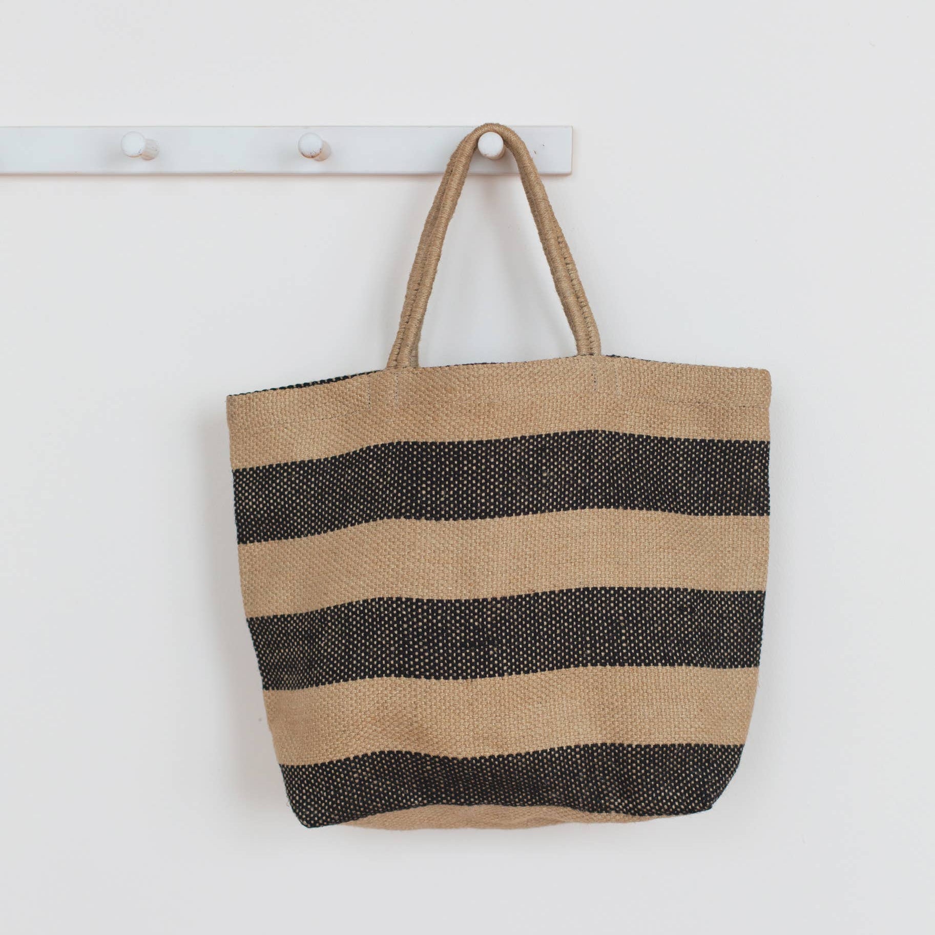 Striped tote bag with black and beige stripes hanging on a white wall.