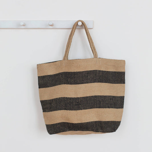 Striped tote bag with black and beige stripes hanging on a white wall.