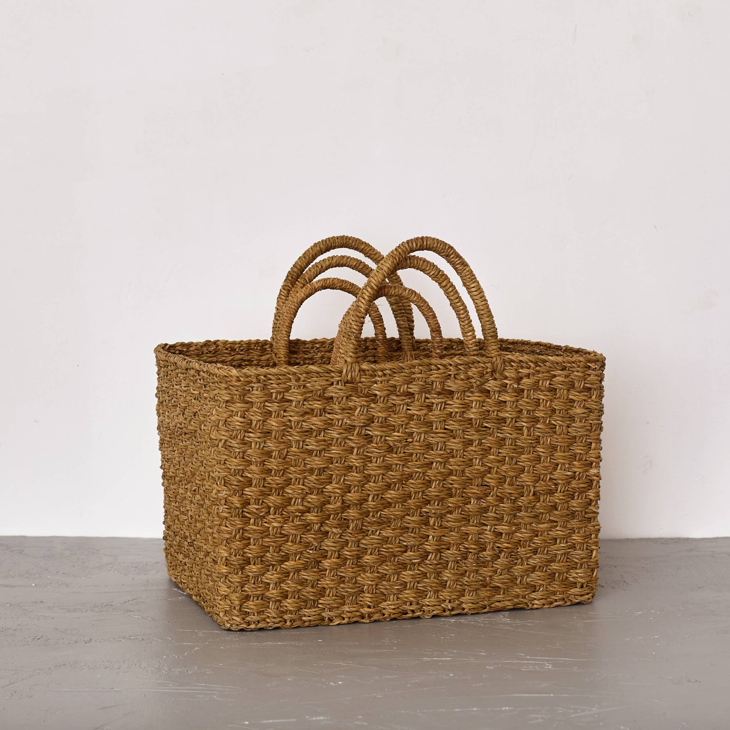 Woven brown basket with handles on a gray surface and white background