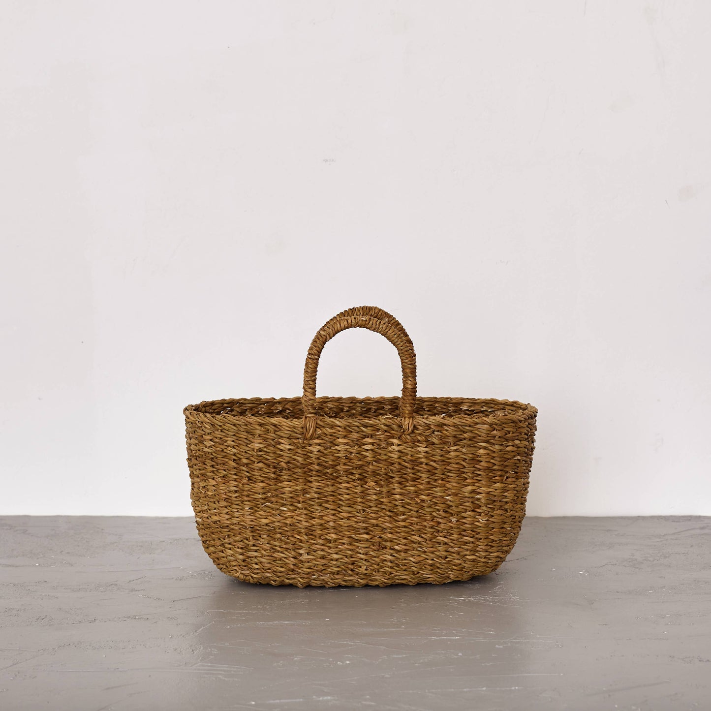 Woven basket with handles on a gray surface and white background