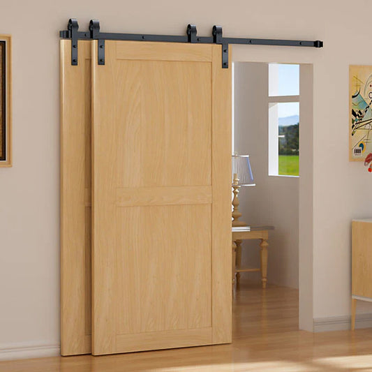 A light natural wood sliding barn door with black metal hardware, shown installed in a doorway of a room with beige walls and wood flooring.