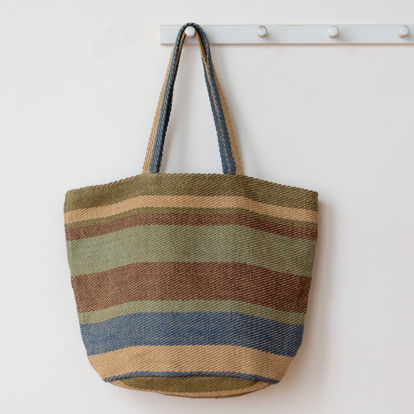 Striped tote bag hanging on a white wall with a coat rack.