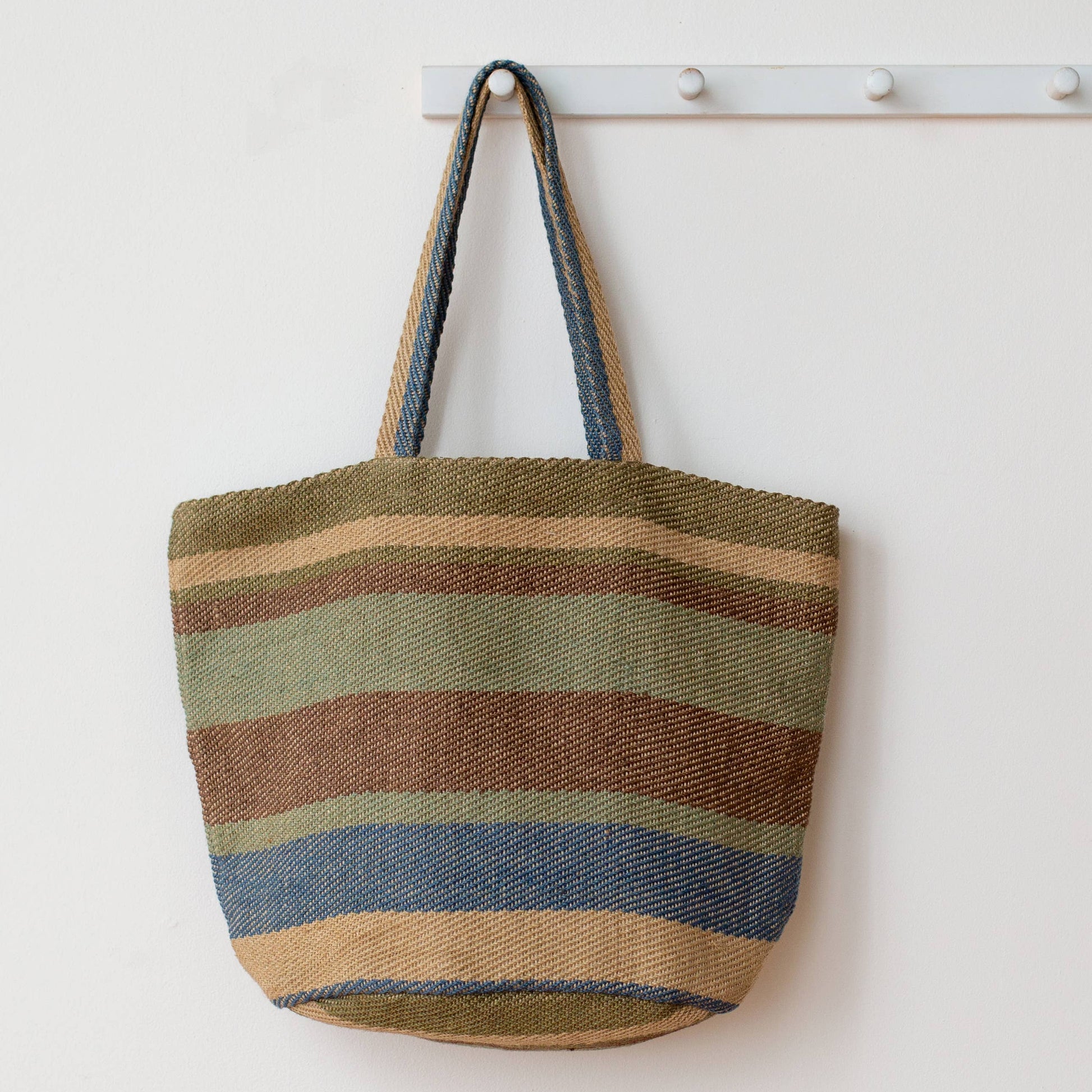 Striped tote bag hanging on a white wall with a coat rack.