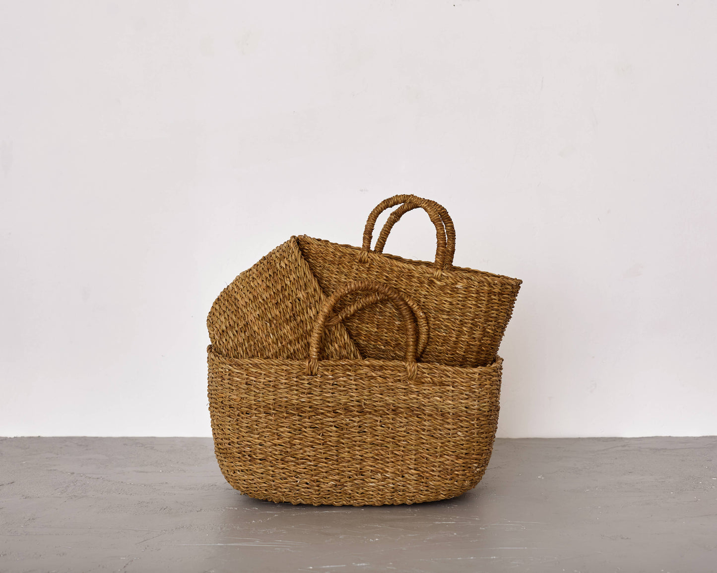 Woven basket with handles on a gray surface against a white background