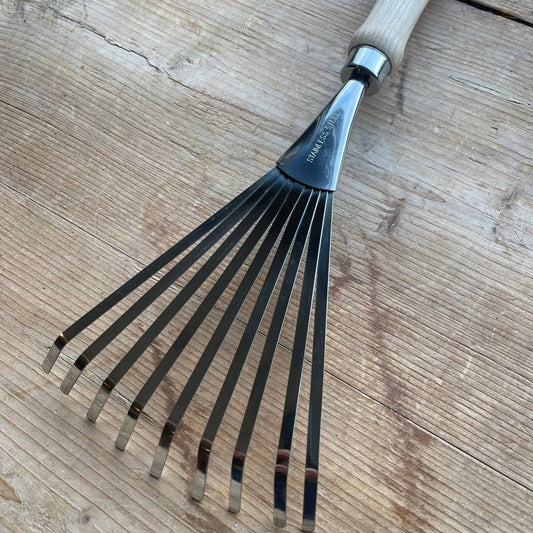 Gardening tool, specifically a rake with a wooden handle, on a wooden surface.