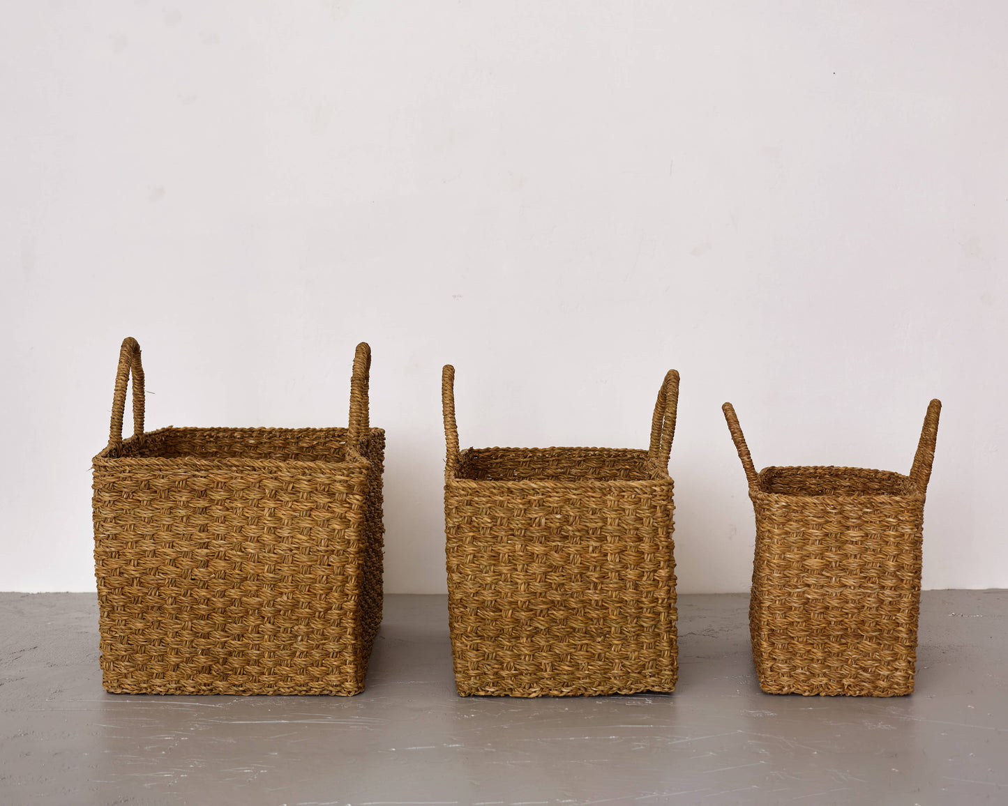 Three woven baskets of different sizes on a plain surface with a white background